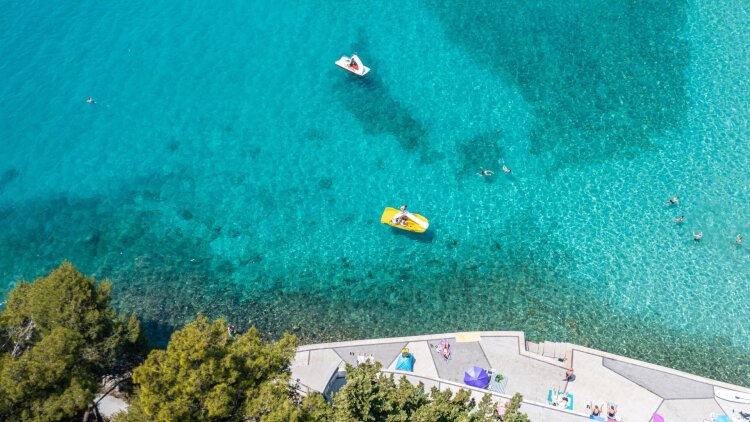 Aerial view of turquoise sea and a beach on Krk island, with pedal boats and swimmers