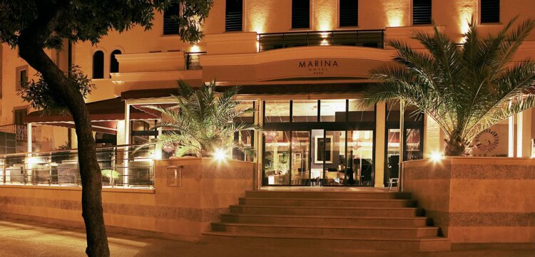 Entrance to Boutique Hotel Marina in the center of Krk town at night, with palm trees in front. 