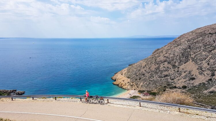 A cyclist on a coastal road overlooking Oprna Bay near Stara Baška, with turquoise waters