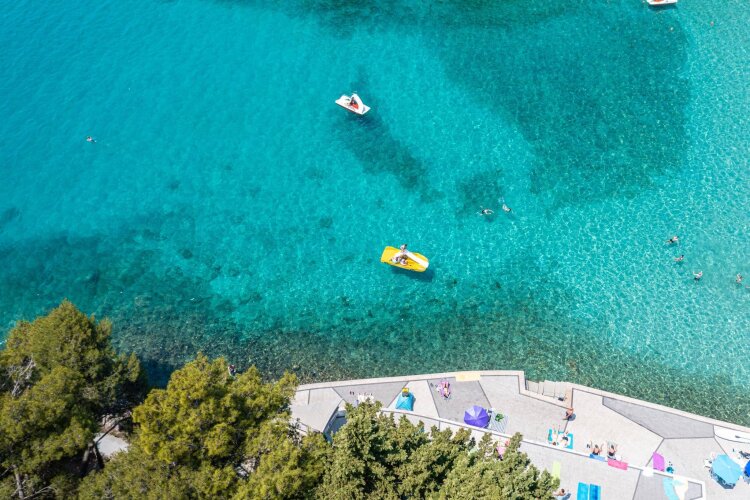 Pogled iz zraka na plažu s kristalno čistim morem i pedalinama pokraj drveća