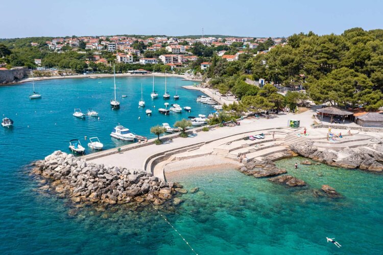 Aerial view of a harbor with boats, a seaside promenade, and a Krk town.