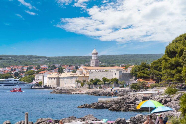 View of the Krk old town, rocky beach and a harbour with boats