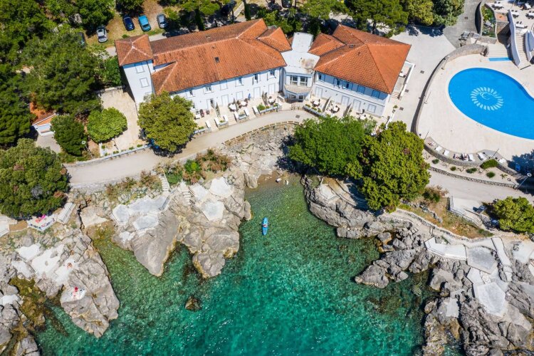 Aerial view of a Hotel Resort Dražica with a rocky cove, turquoise sea, and an outdoor pool.
